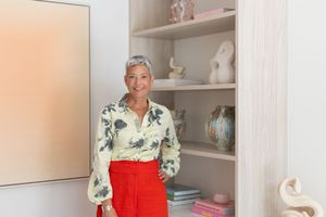 A person in a bright red dress stands in a modern white kitchen with built-in shelving and decorative items.