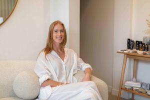 Relaxed practitioner in white clothing sitting on cream couch in modern wellness space.