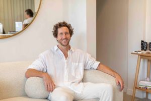 Wellness professional in casual white attire seated on light colored sofa in modern clinic.