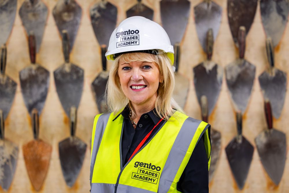Woman in high-visibility gear and a hard hat standing in front of a display of masonry trowels at a construction training facility.