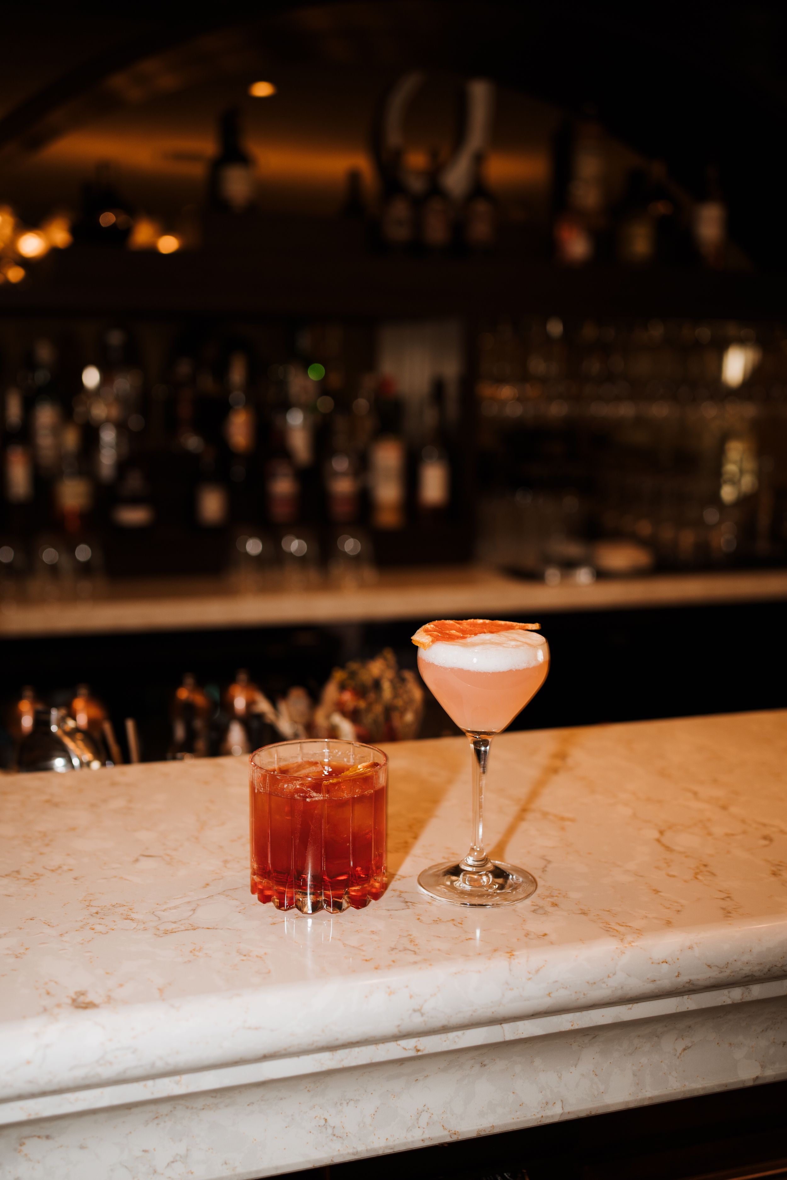 Two craft cocktails on a marble bar counter in warm ambient lighting at the ned, London