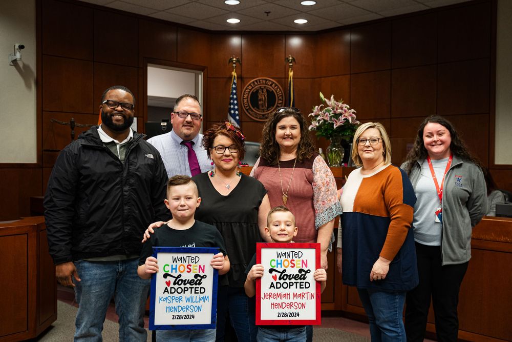 Group photo of family adoption celebration in courthouse with signs and smiles.