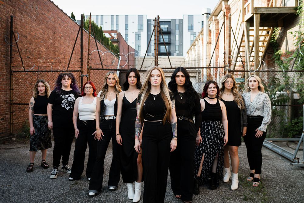 Group portrait of women wearing black and white outfits in urban alley setting.