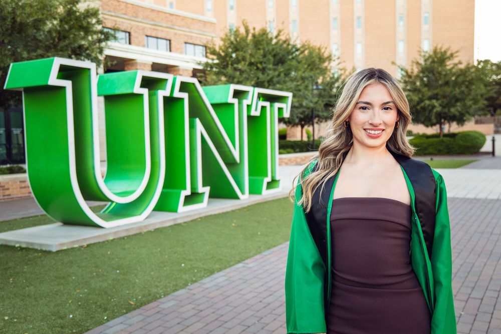 Large green UNT letters displayed on campus grounds with brick building backdrop.