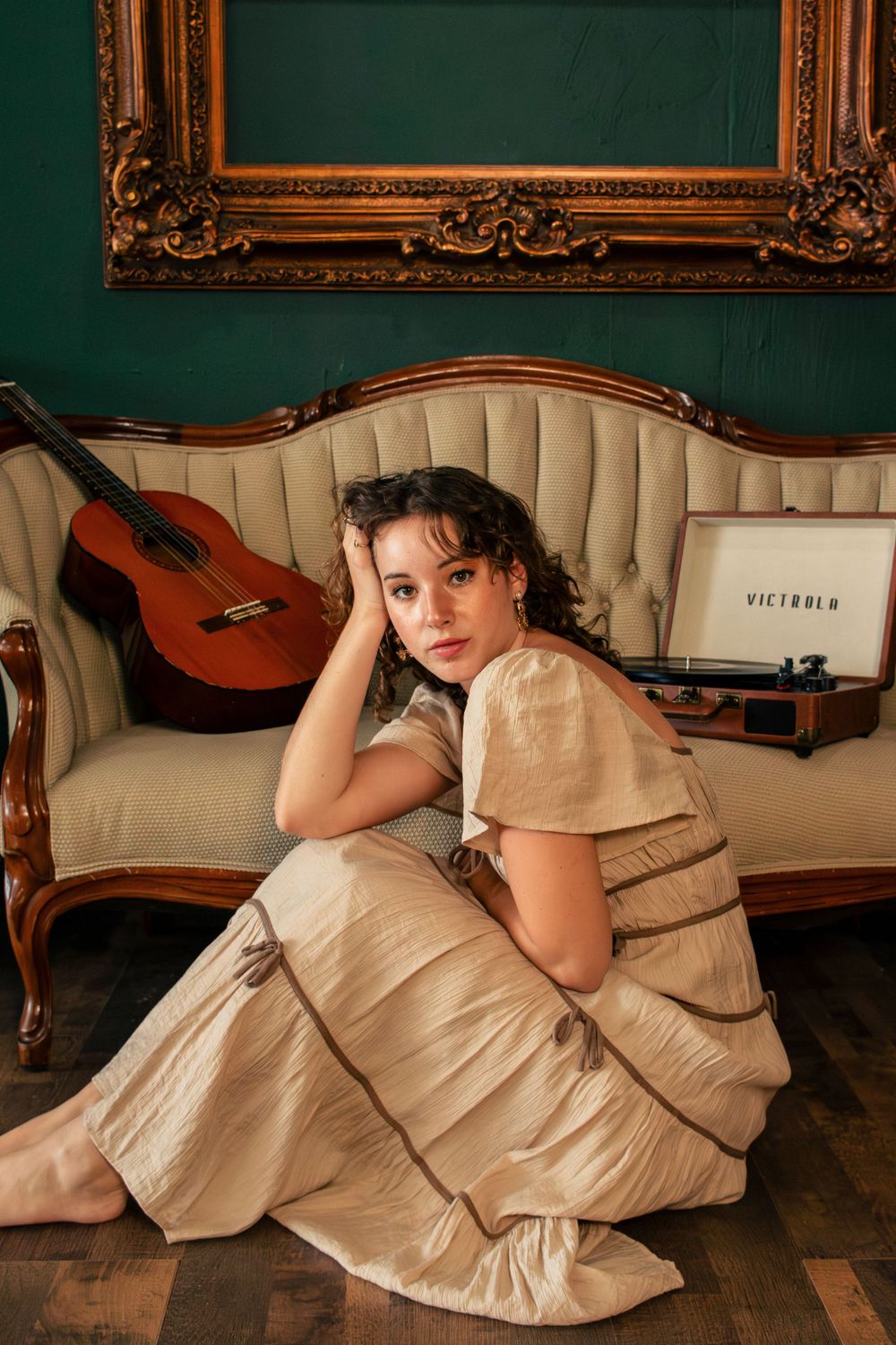 Girl sits on the floor in front of a couch with a record player and a guitar behind her on the couch