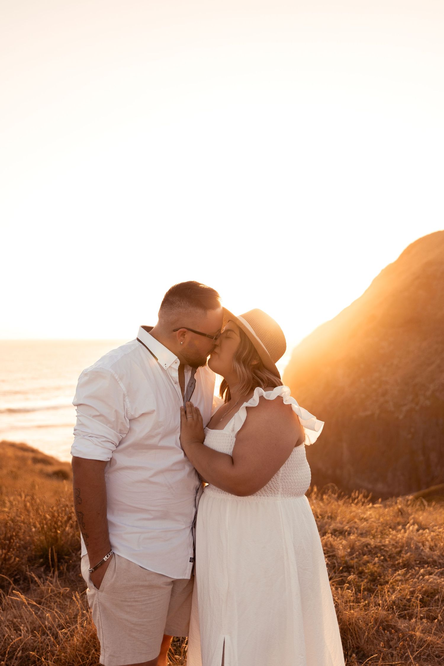 Couple embraces during golden hour sunset by the ocean.
