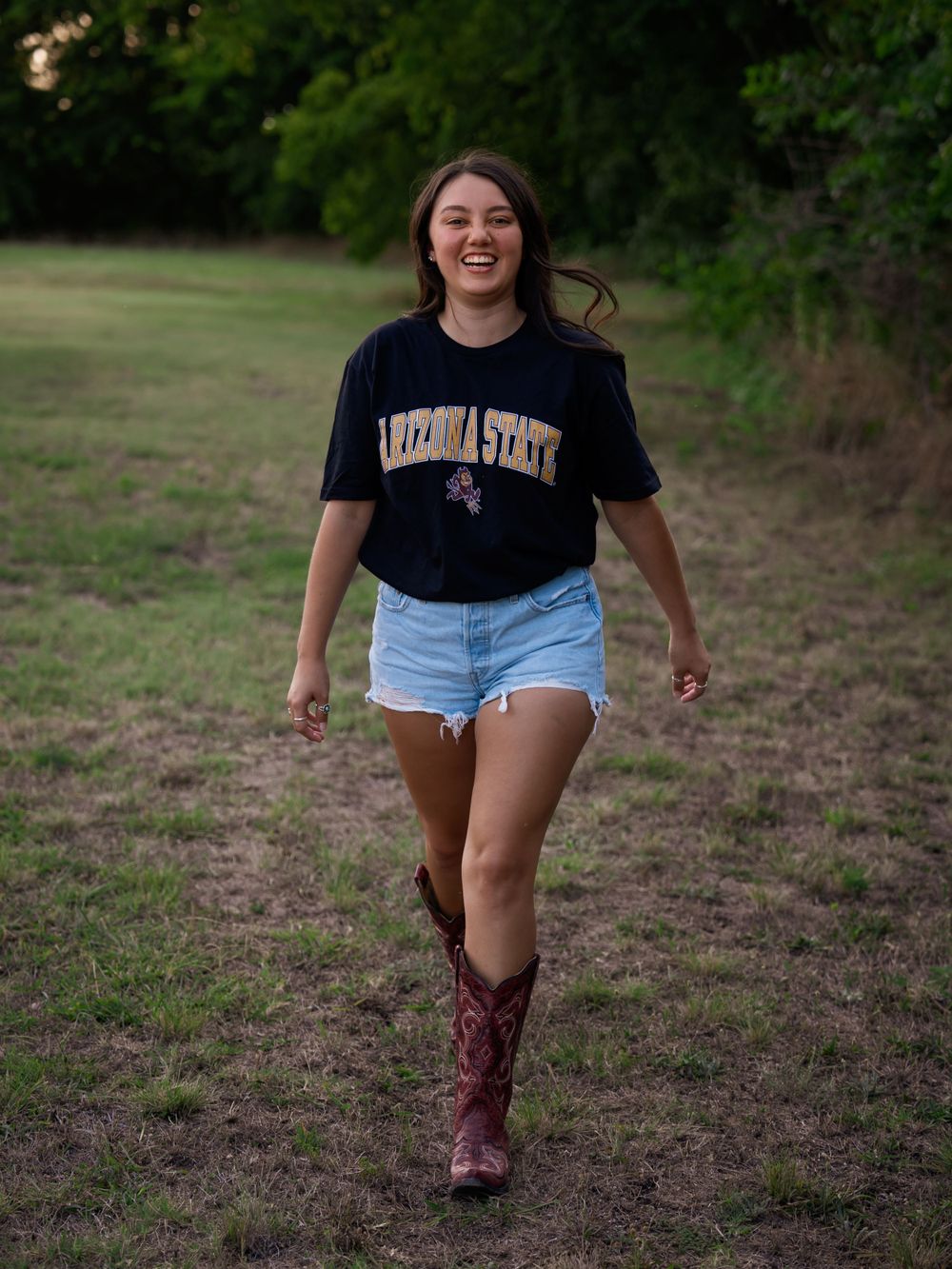 Person in college shirt and cowboy boots walking joyfully through a field.