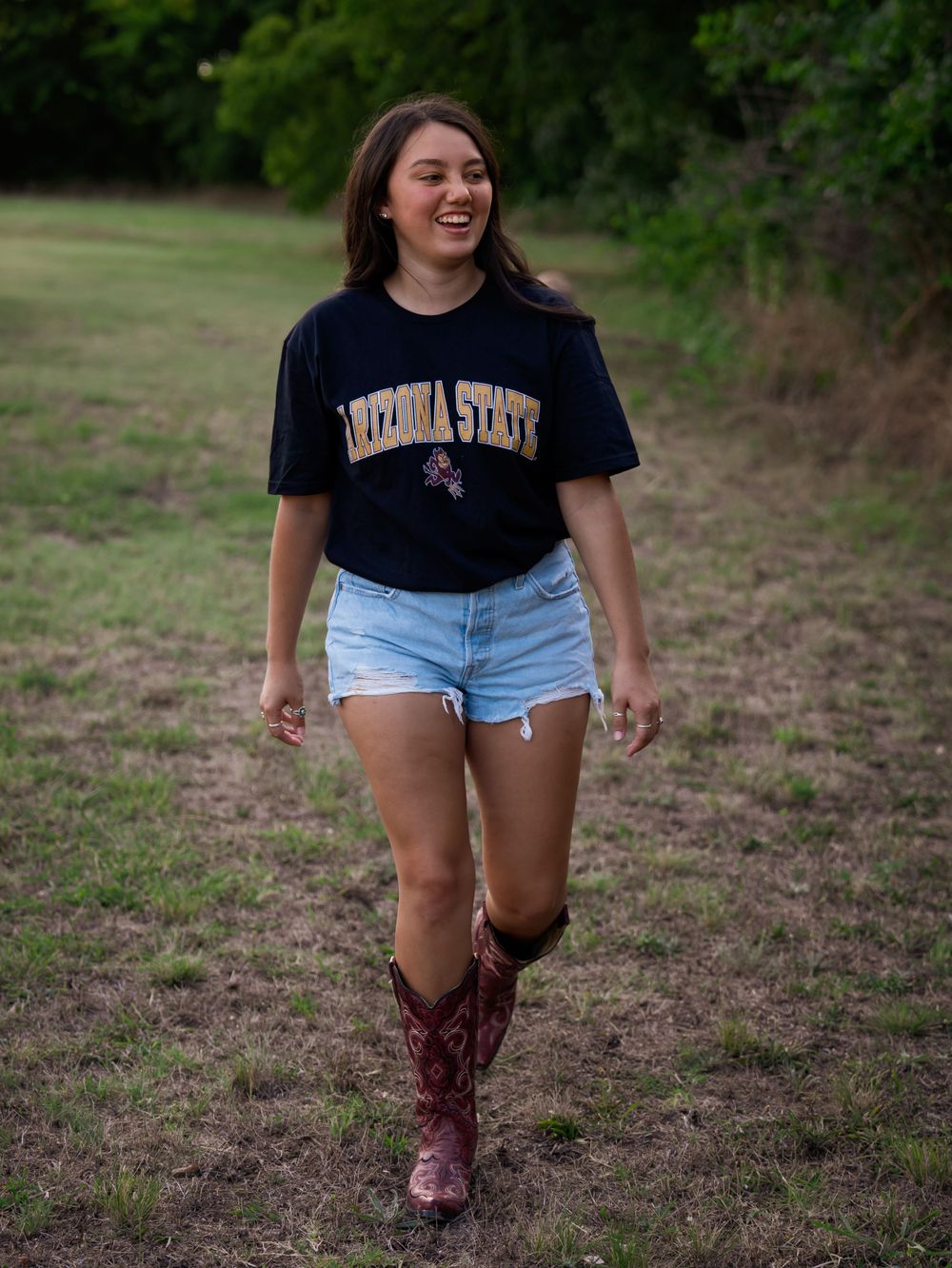 A casual outdoor photoshoot featuring someone in a college t-shirt, denim shorts and burgundy cowboy boots.