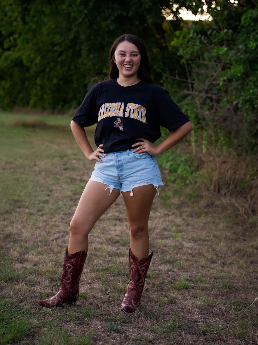 Energetic pose in an outdoor setting wearing western boots and a university t-shirt.