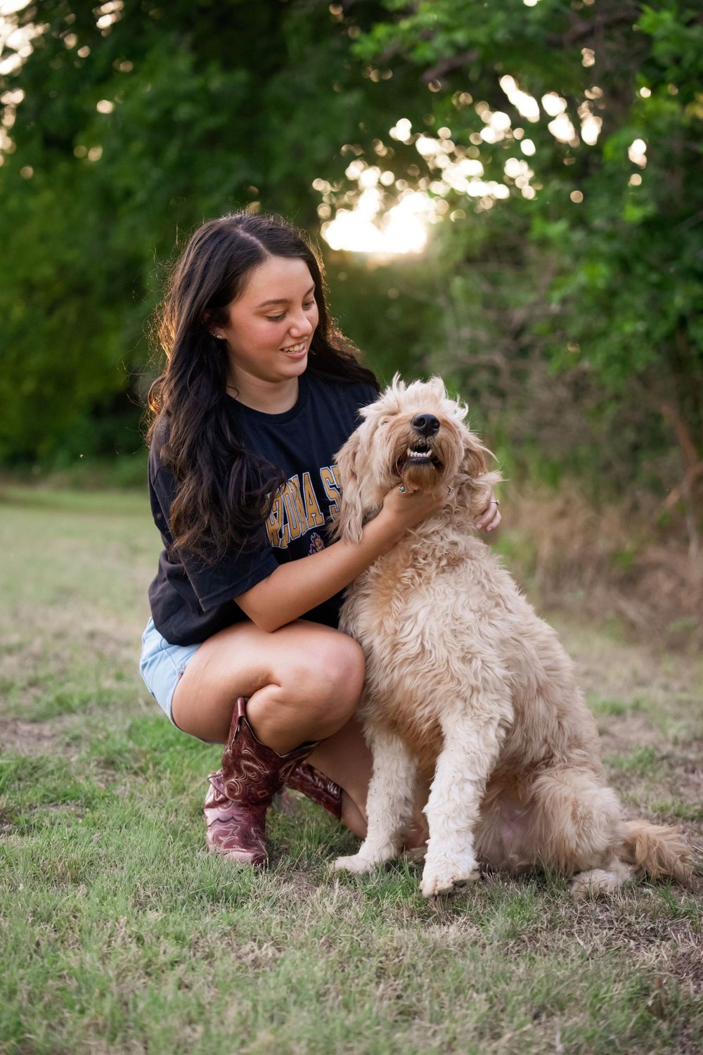 Kneeling down to pet a friendly goldendoodle dog while wearing western boots and denim shorts.