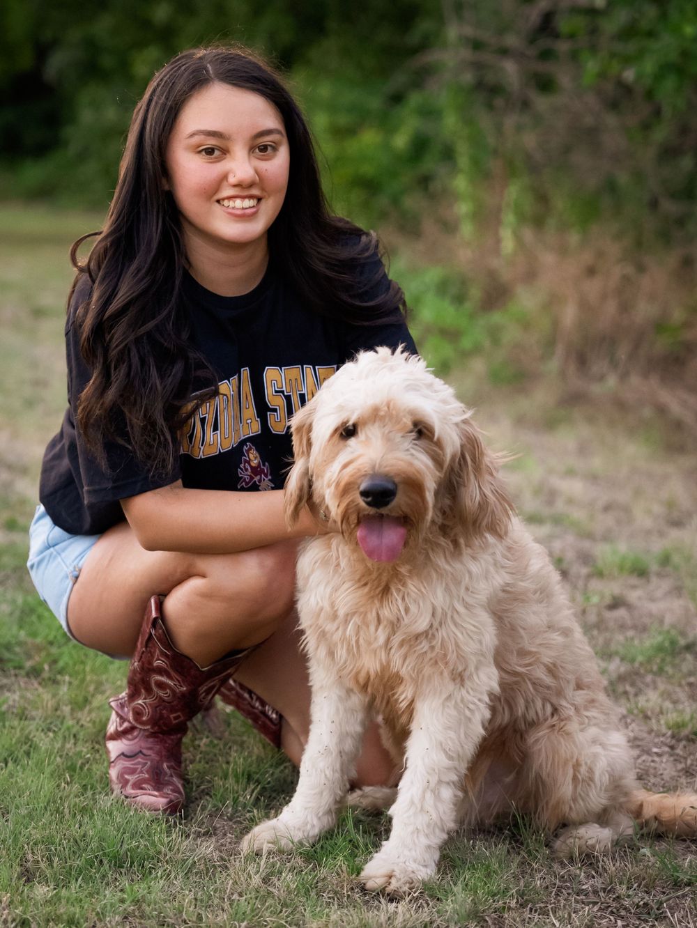 Outdoor portrait with a friendly goldendoodle dog featuring western boots and a university shirt.