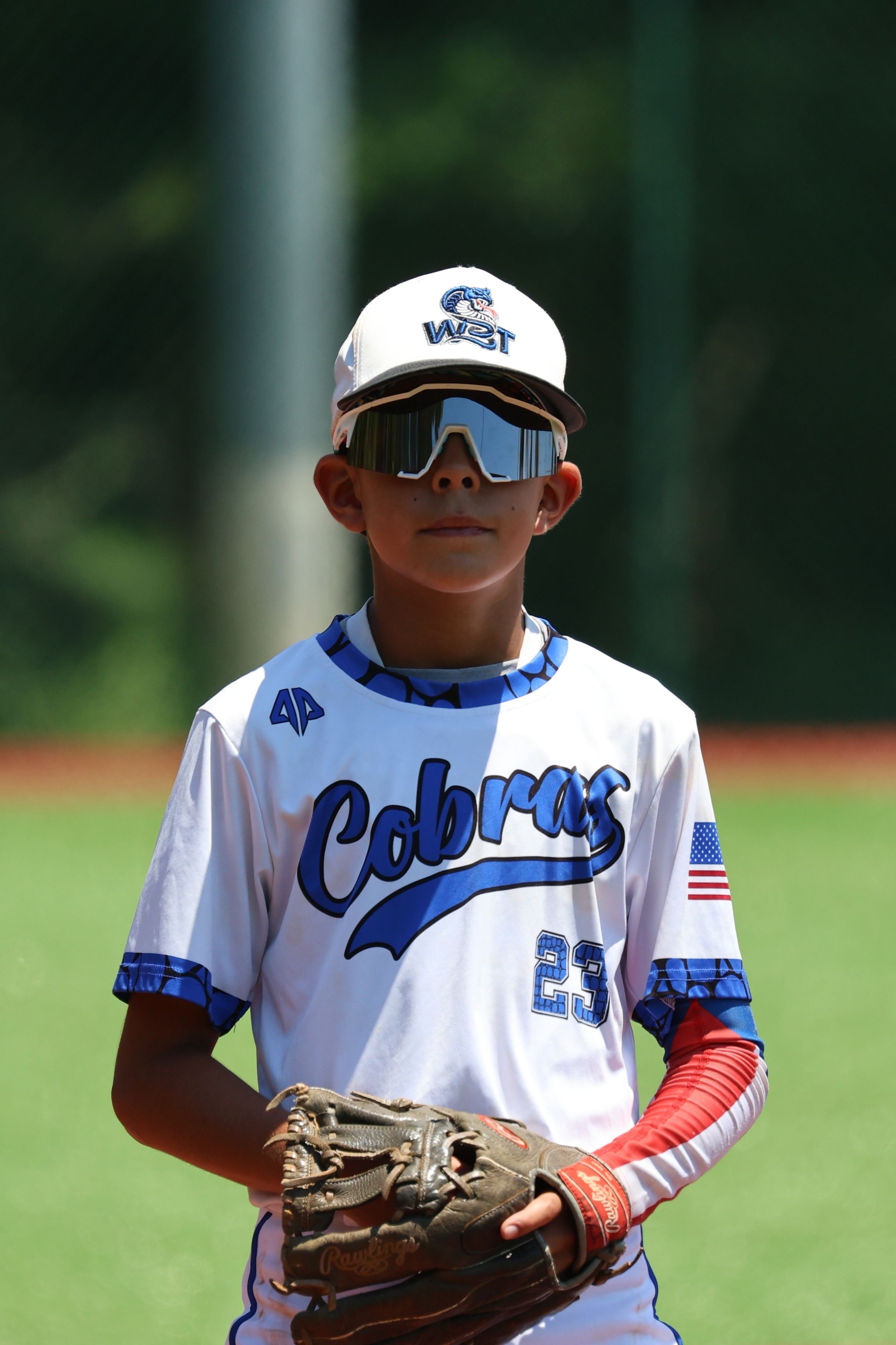Youth baseball player in Cobras uniform stands ready with glove on sunny field.