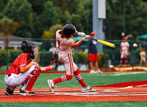 Baseball batter in red and white uniform swinging at pitch while catcher crouches behind home plate.