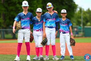 Four youth baseball players in uniforms with pink socks standing together on the field.