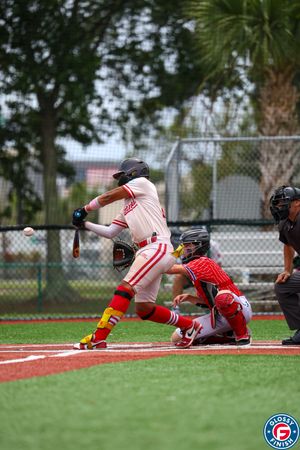 Baseball batter in white and red uniform at bat while catcher squats behind home plate.