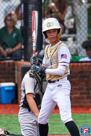 Baseball batter in white and gold uniform preparing to hit at home plate.