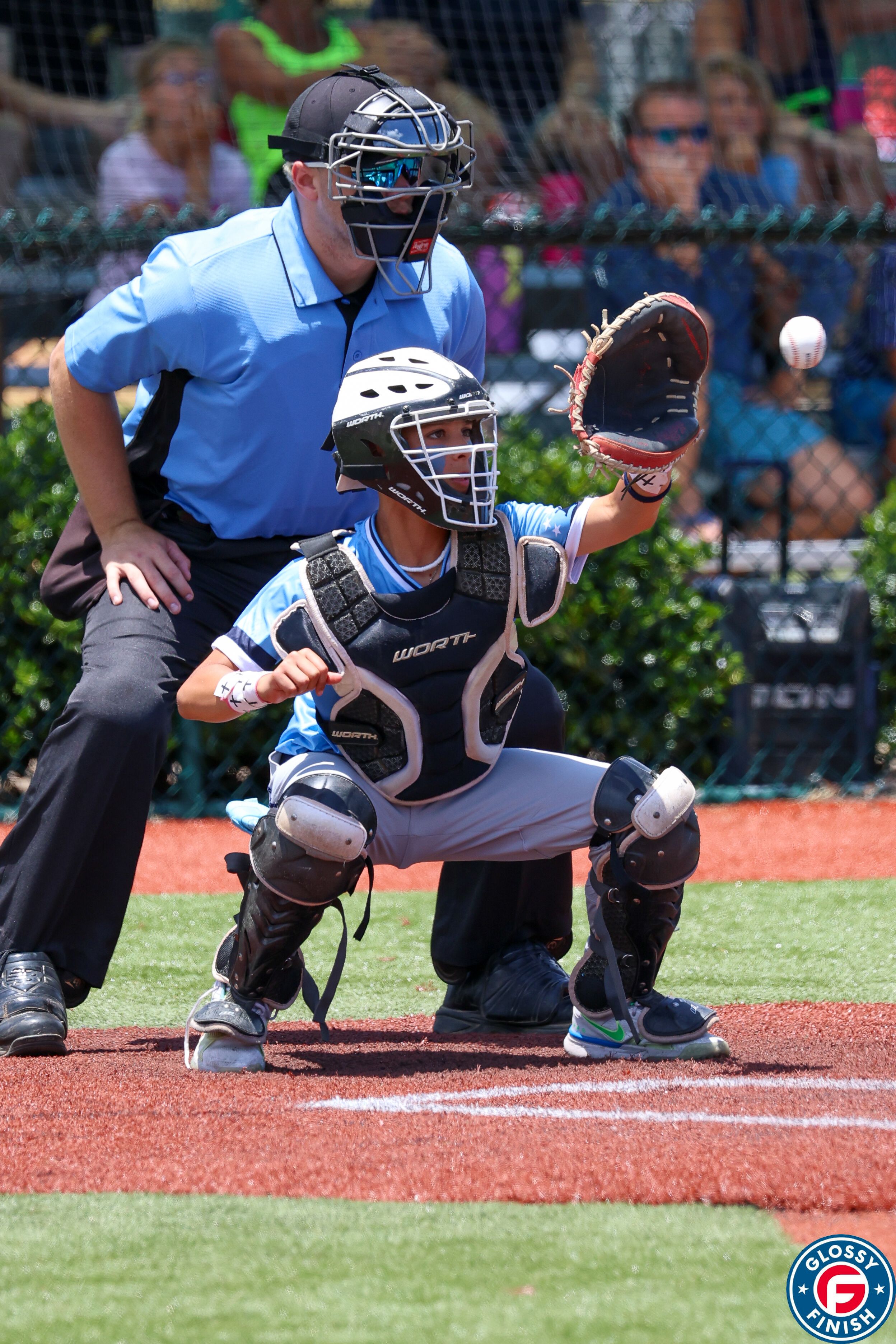 A baseball catcher in protective gear drops low to block a ball at home plate during a game.