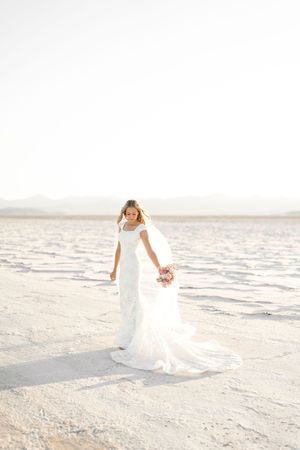 A person in an elegant white wedding dress twirls gracefully on a pristine sandy beach at sunset.