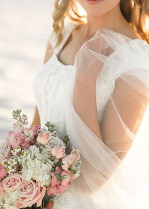 Soft pink and white rose bouquet with delicate tulle veil detail in golden sunlight.
