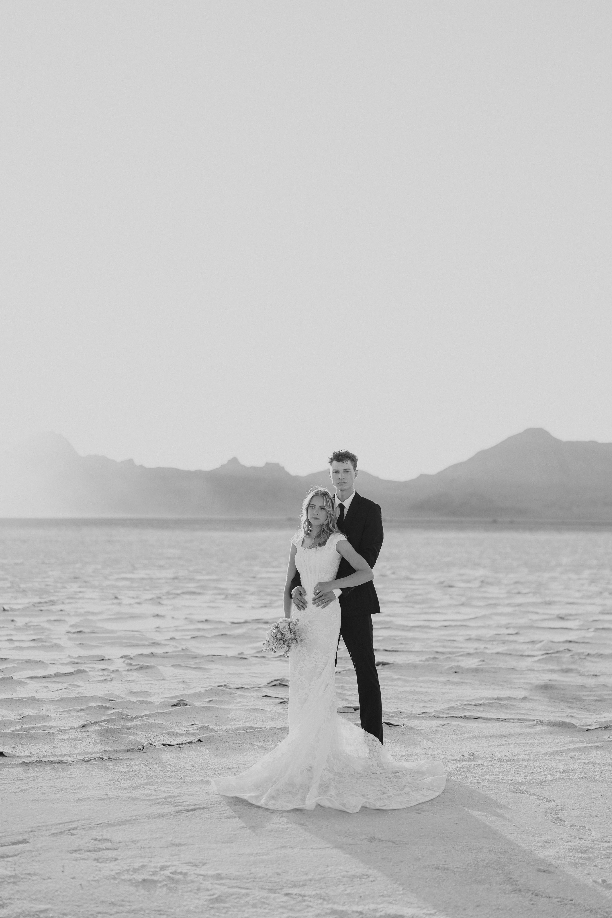 A romantic beach wedding photoshoot showing a couple dancing together on the salt flats at sunset with mountains in background.