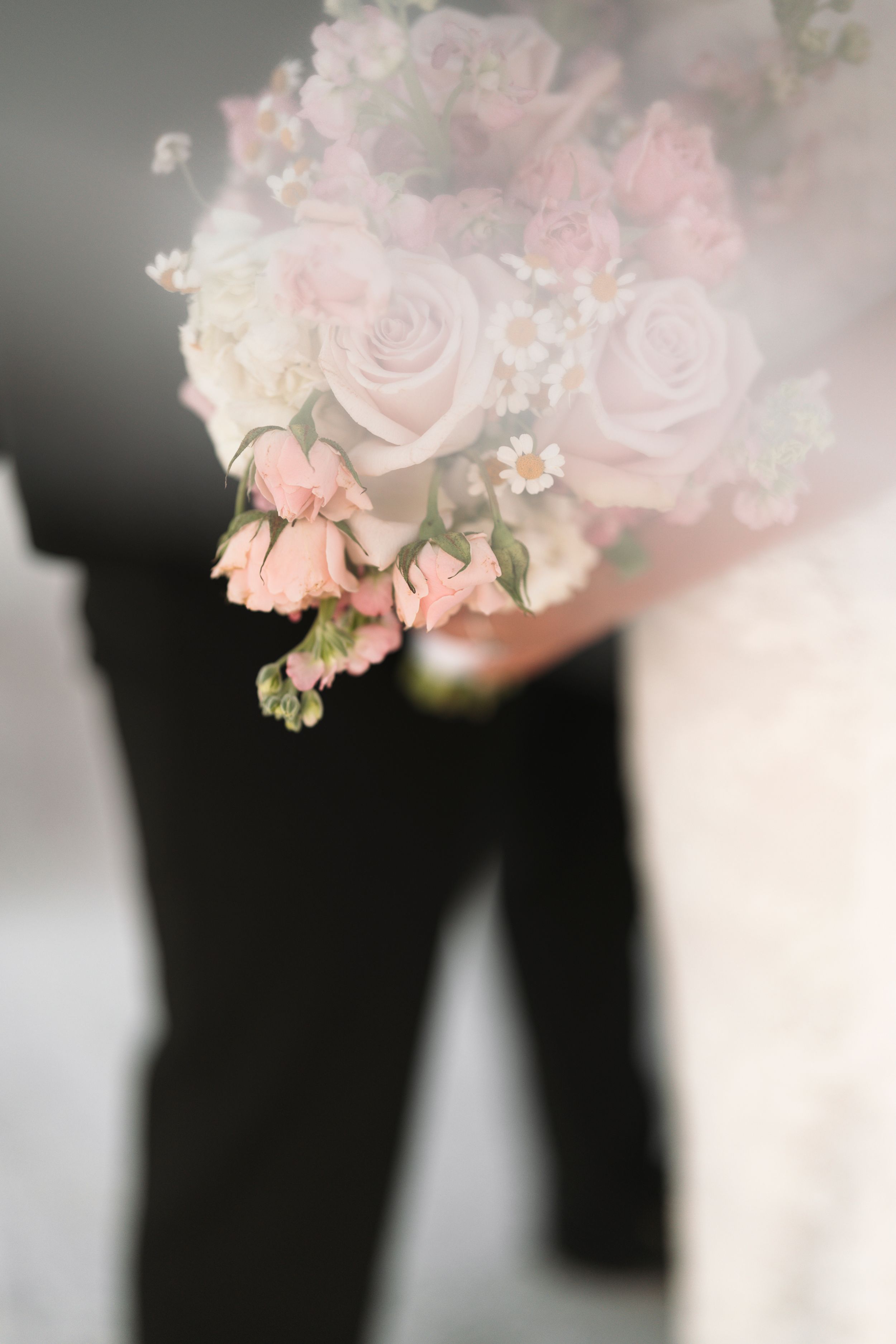 Pink roses and delicate white flowers create a soft, romantic arrangement against a dark background with elegant bokeh effect.