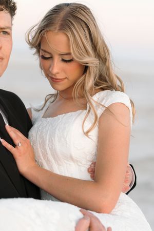 A bride in a white wedding dress with blonde wavy hair gazes down while wearing elegant bridal attire.
