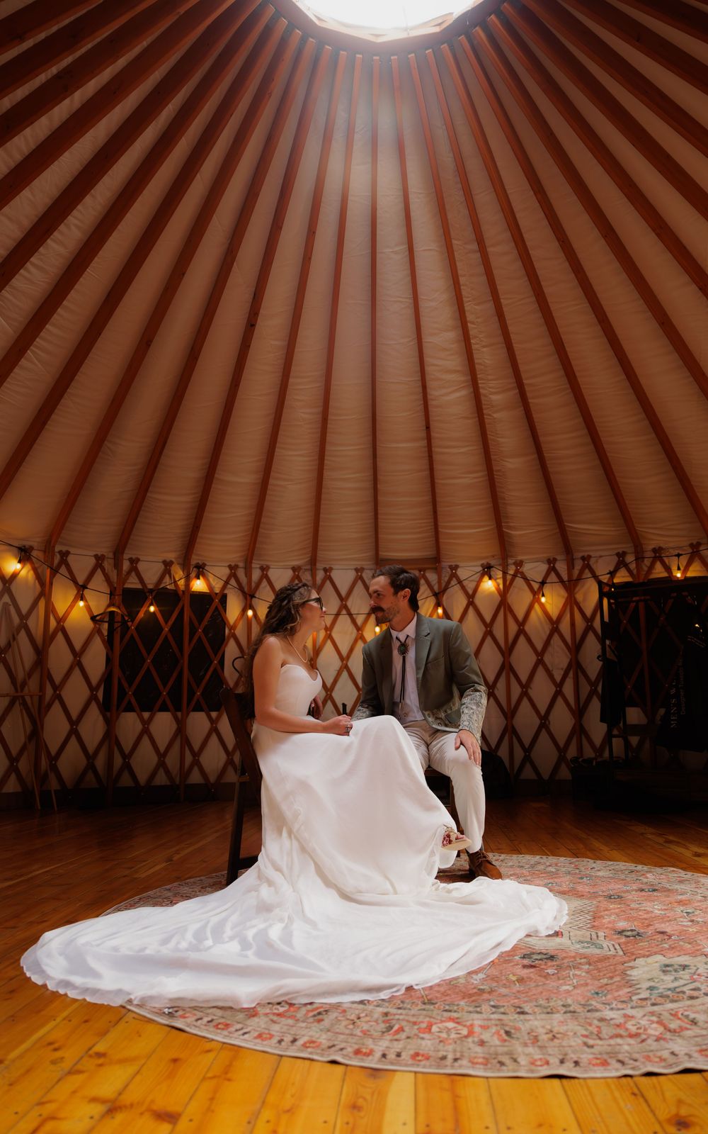 Bride and groom share a romantic moment inside a rustic yurt wedding venue with warm string lights and wooden floors.
