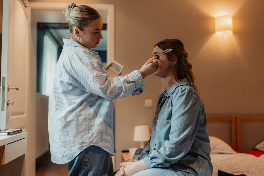 A makeup application session taking place in a warmly lit bedroom setting.
