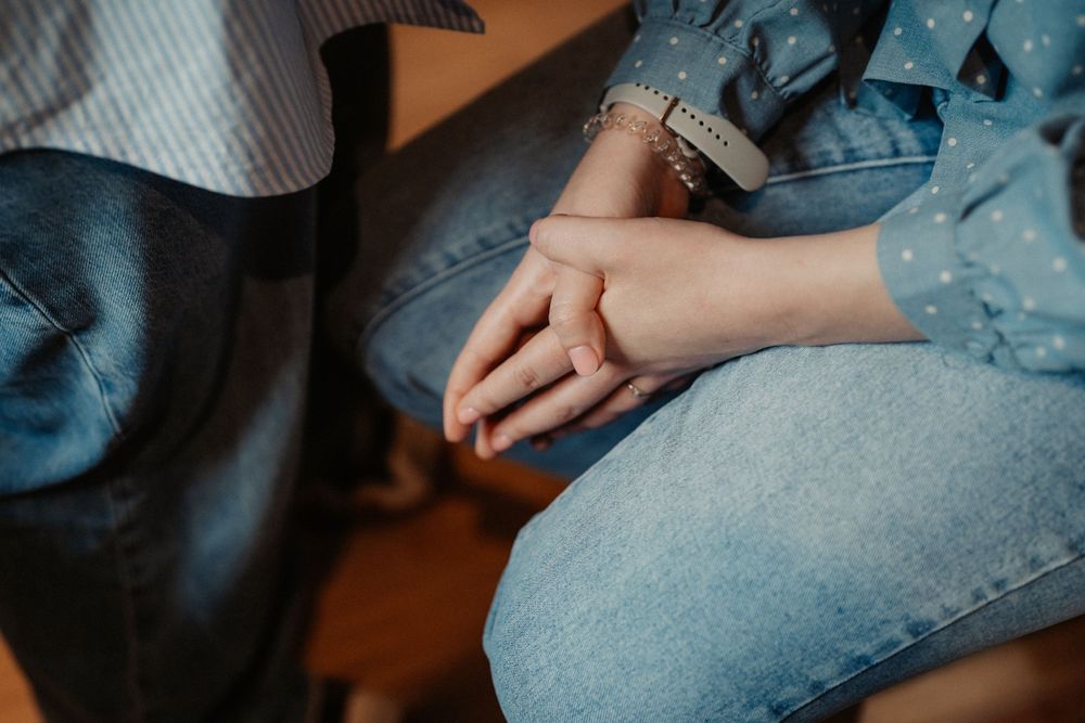 Close-up view of hands resting on denim-clad legs in natural indoor lighting.