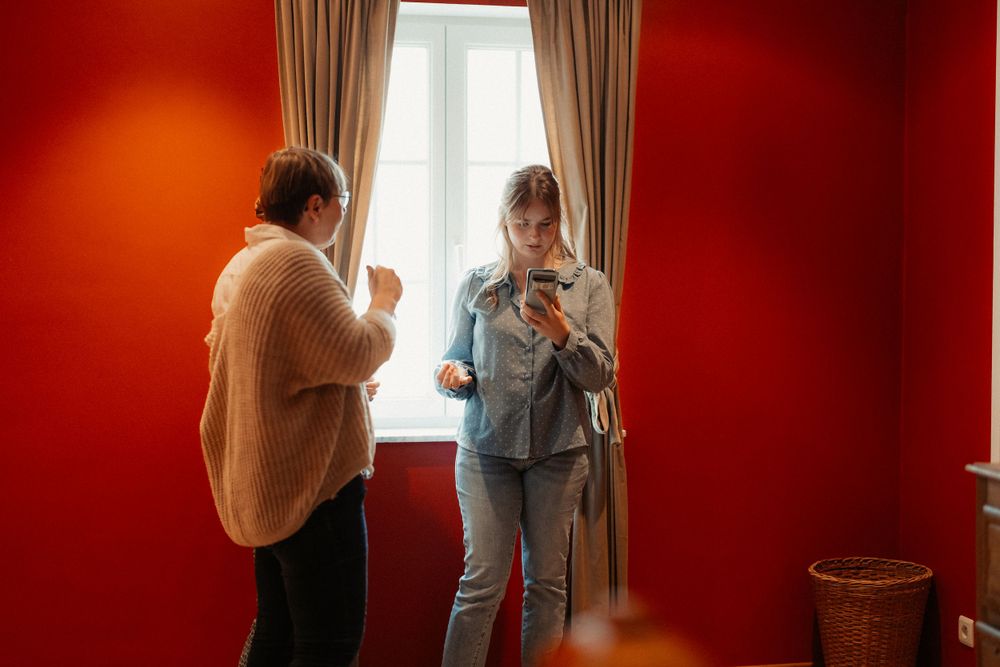 Two people conversing in a room with vibrant red walls and natural window light.