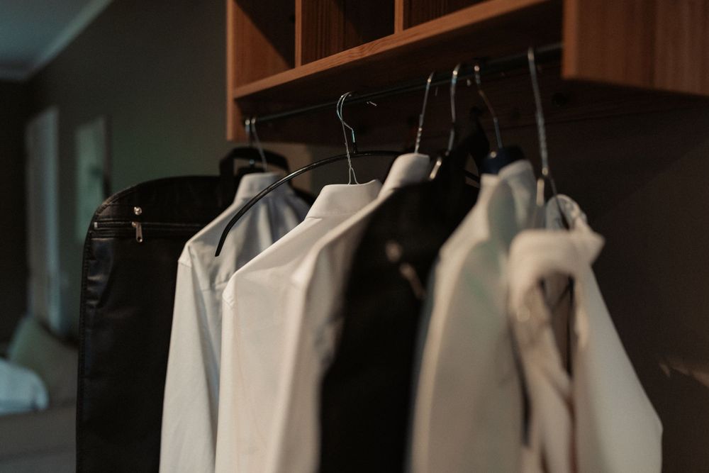 A row of black and white formal clothing hanging on wooden closet shelves.