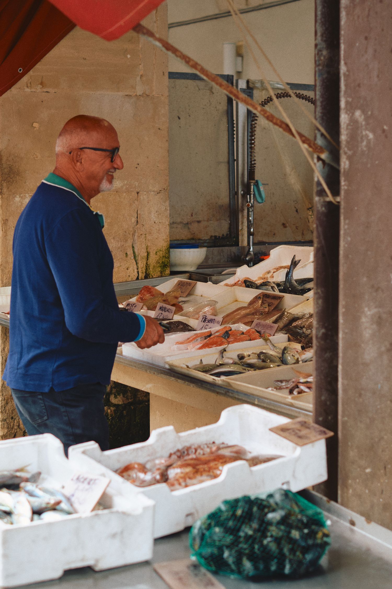 A fishmonger arranges fresh seafood at a market stall with white display containers.