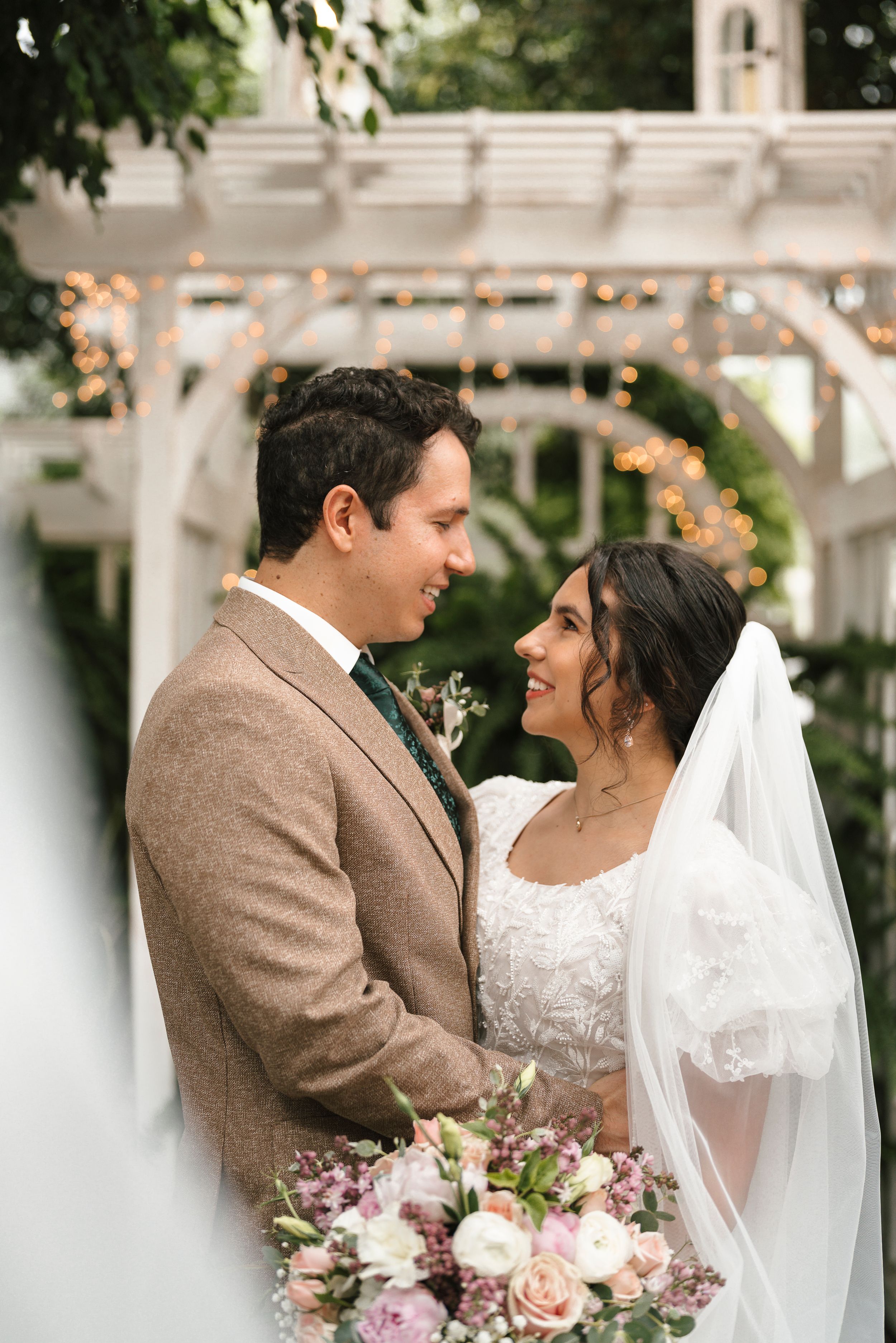 A wedding couple share an intimate moment outdoors with romantic lighting and pink rose bouquet decorations.
