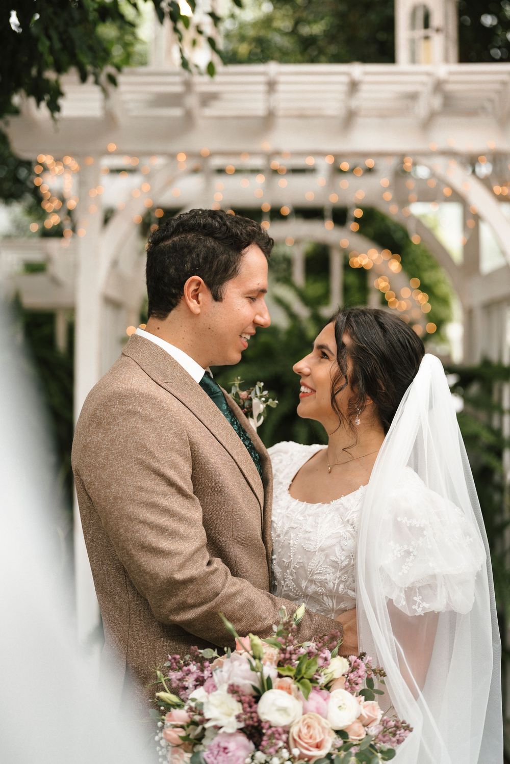 A wedding couple share an intimate moment outdoors with romantic lighting and pink rose bouquet decorations.