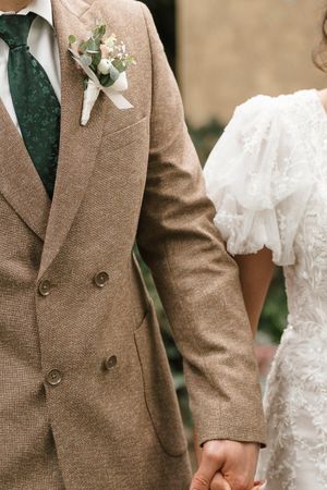 A detail shot shows hands holding in a wedding ceremony with brown tweed suit sleeve and white lace dress details.