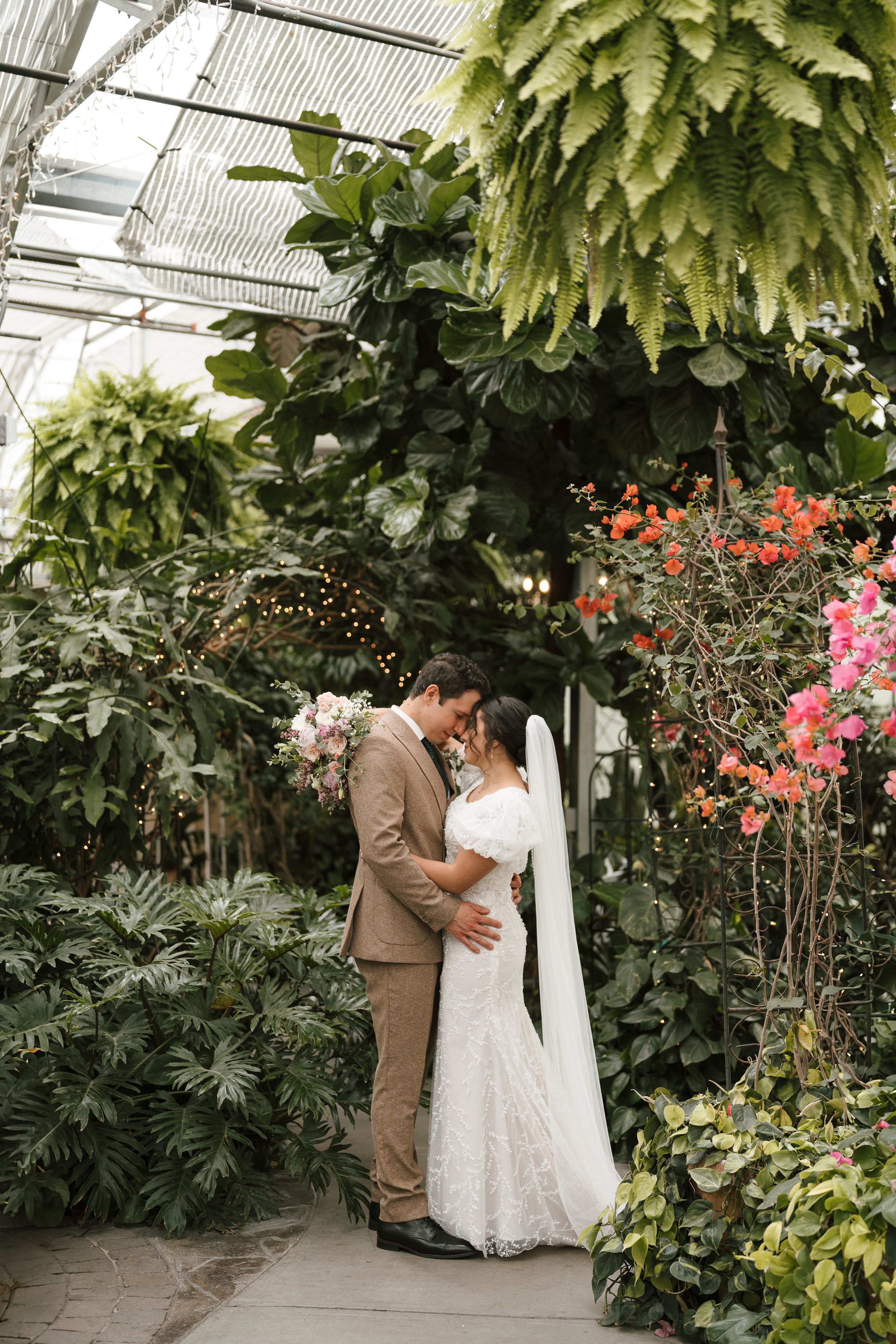 A romantic greenhouse wedding portrait surrounded by cascading plants, flowering vines and tropical foliage.