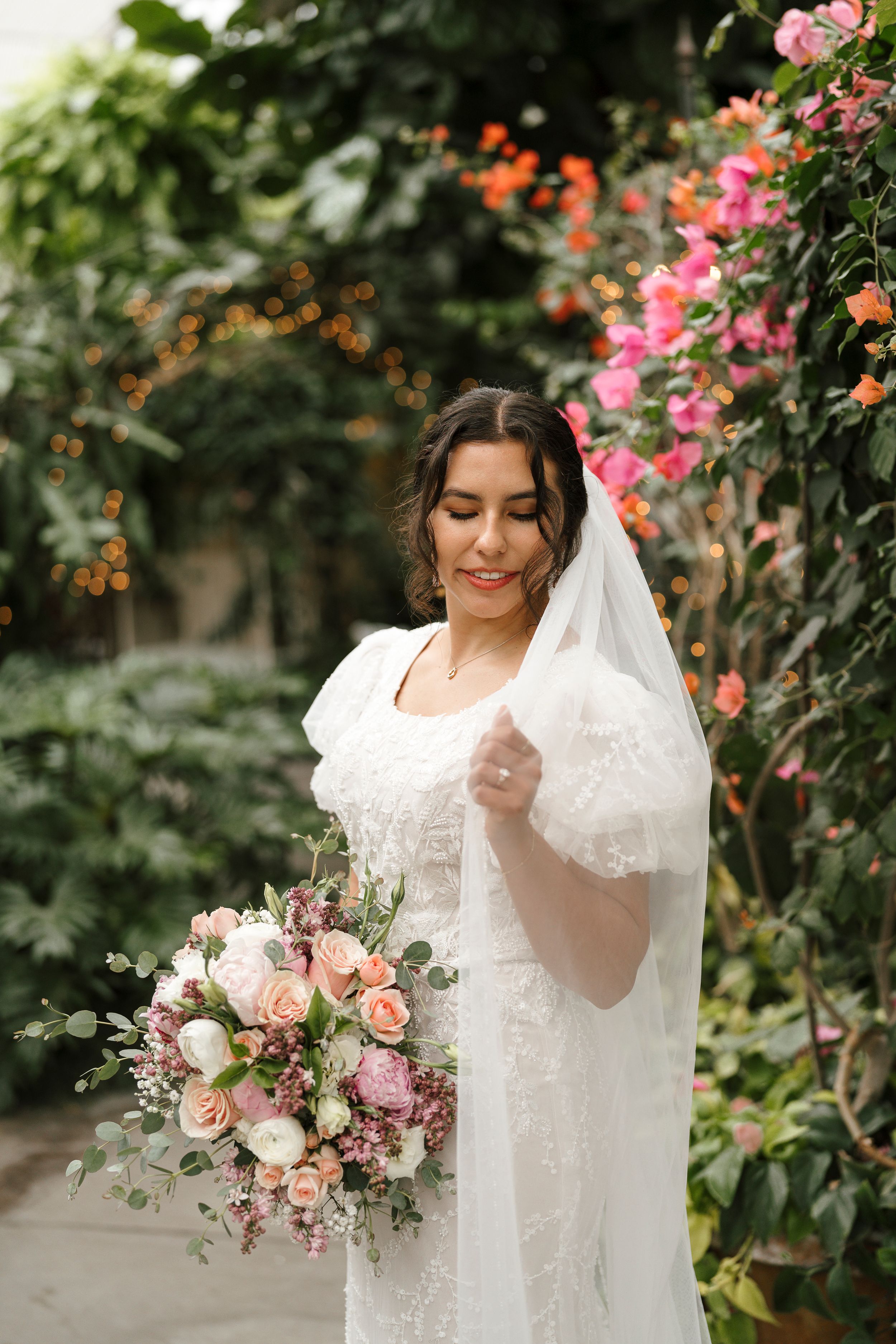 Elegant white lace wedding dress displayed in a garden setting with pink roses and a romantic bouquet.