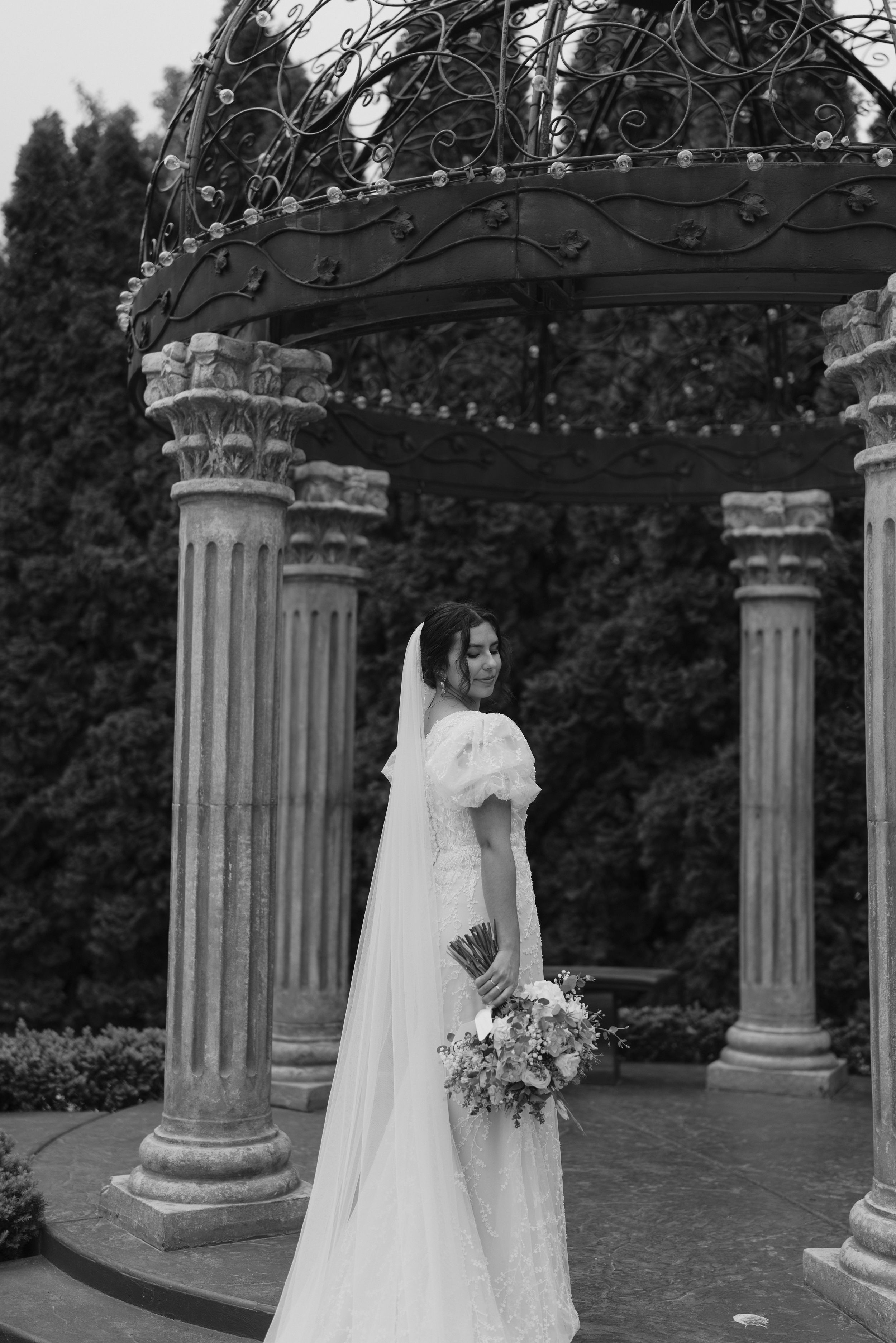 A classic bridal portrait under a decorative iron gazebo with Corinthian columns in black and white.