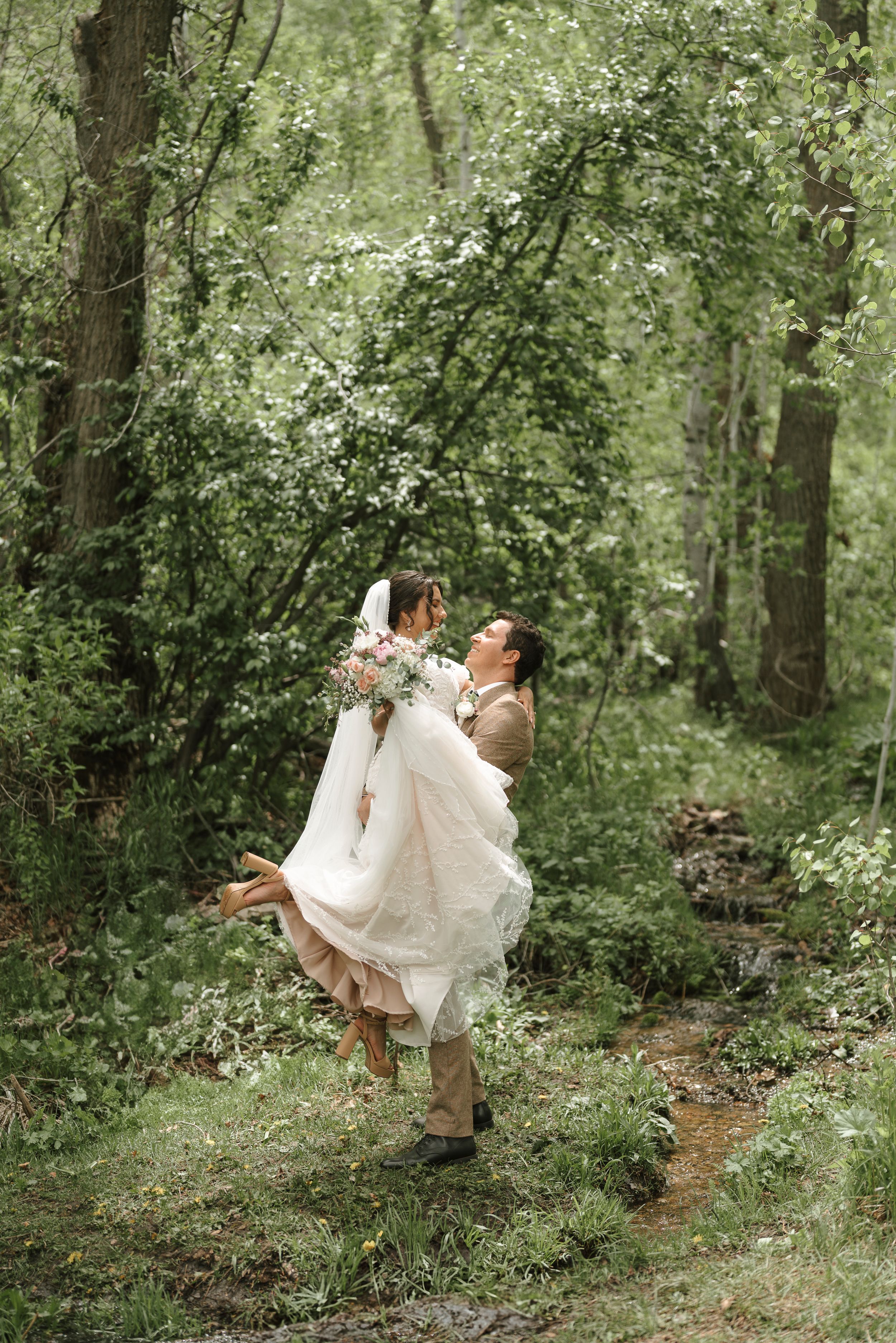 A romantic couple dances together in a lush green woodland setting while wearing beautiful wedding attire.