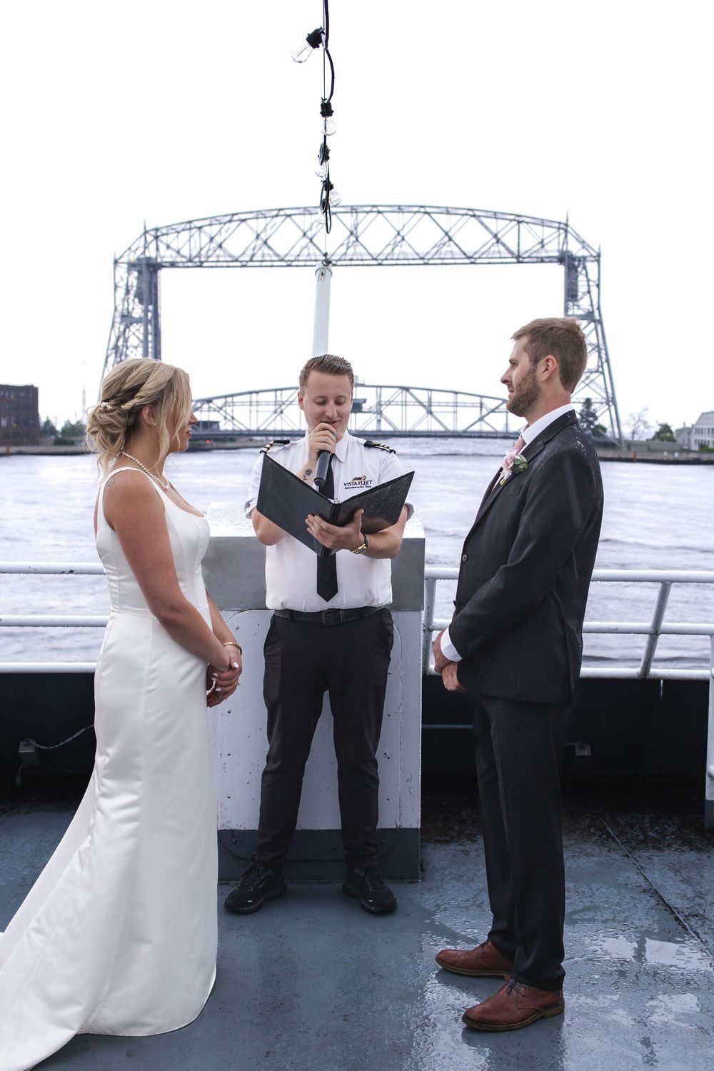 A wedding ceremony takes place on a boat deck with the iconic Duluth Aerial Lift Bridge visible in the background.