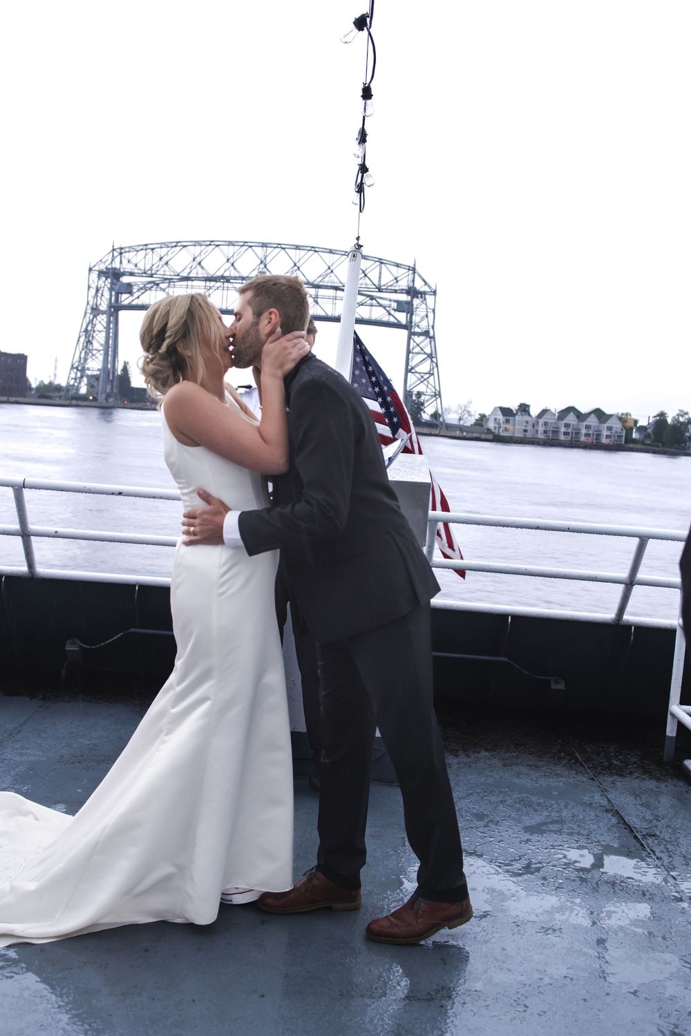 A romantic wedding couple shares a kiss on a boat deck with the iconic Aerial Lift Bridge in Duluth visible in the background.