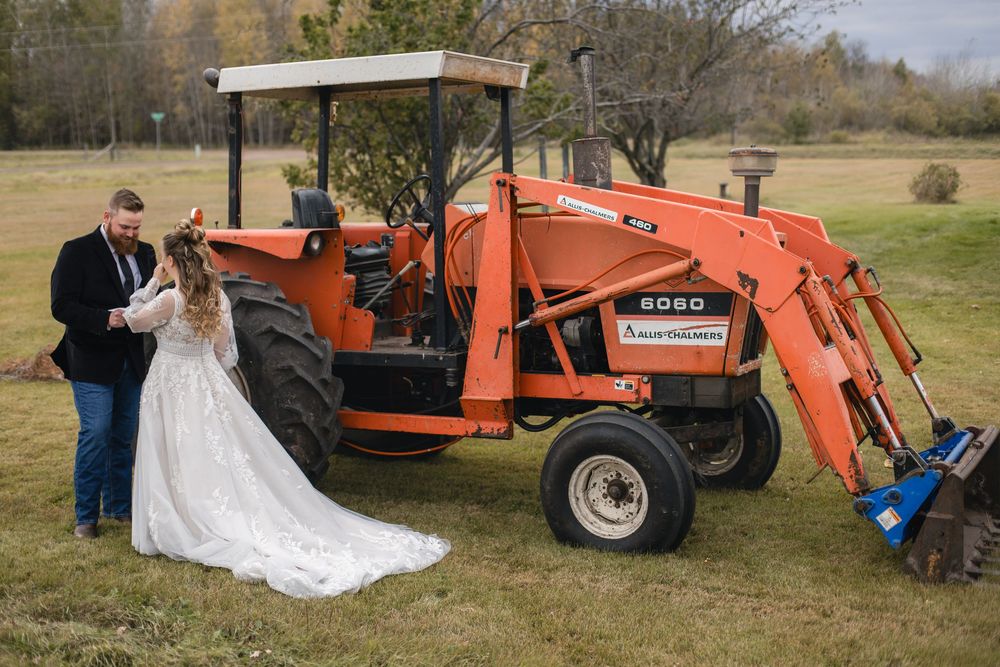 A couple poses with a bright red Kubota tractor in a scenic autumn field during their wedding photoshoot.