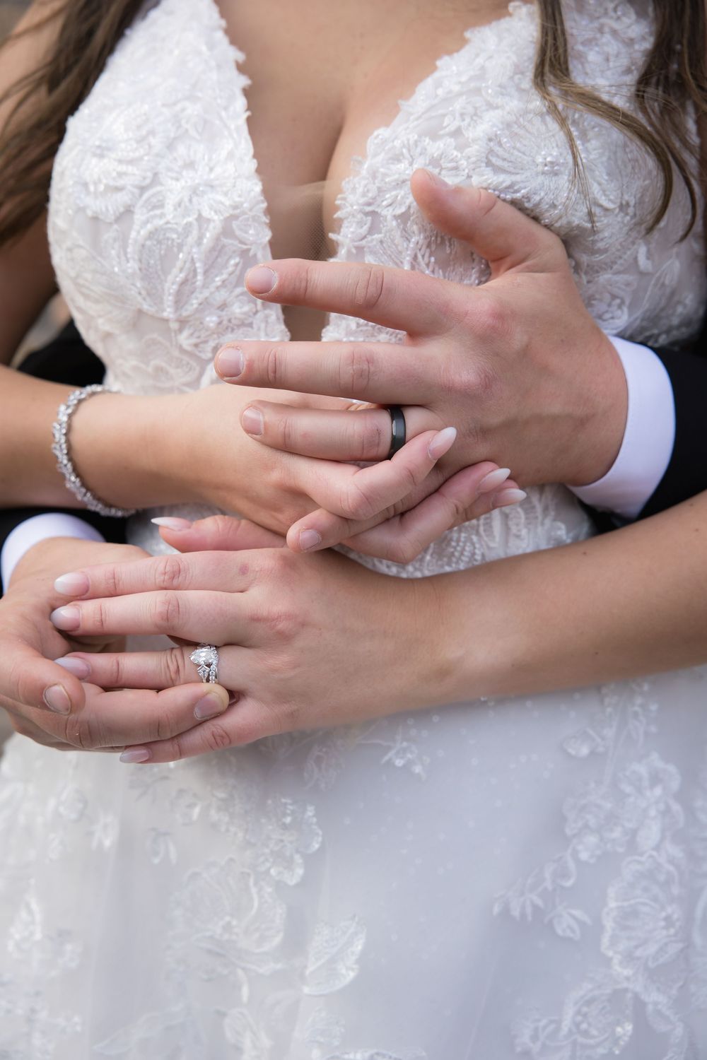 A close-up of hands with wedding rings and white lace dress details.