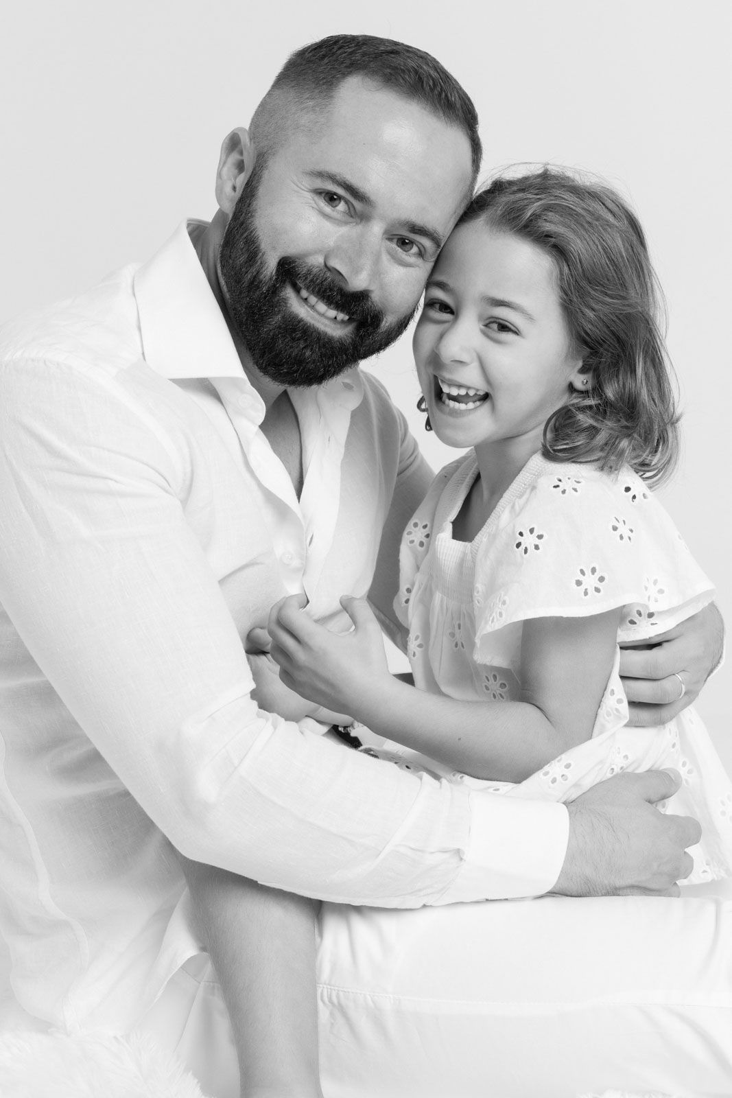 Cadru cu o fetita razand impreuna cu tatal ei intr-un portret de familie minimalist, cu fundal alb.