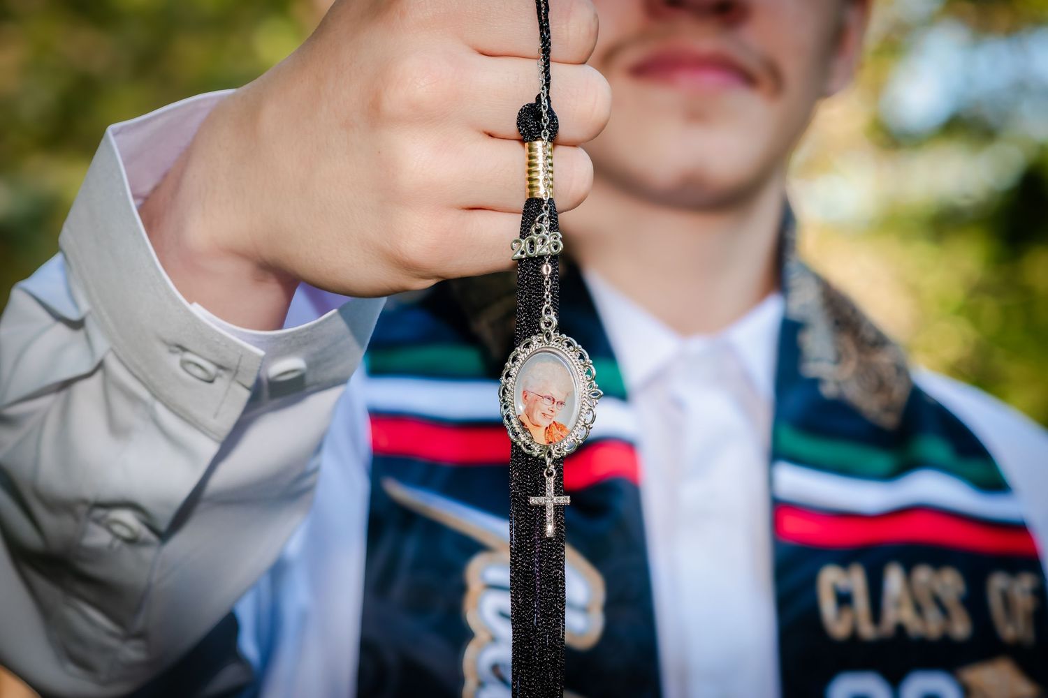 Graduate holding a religious rosary with cross pendant and saint medallion, wearing a colorful graduation stole.
