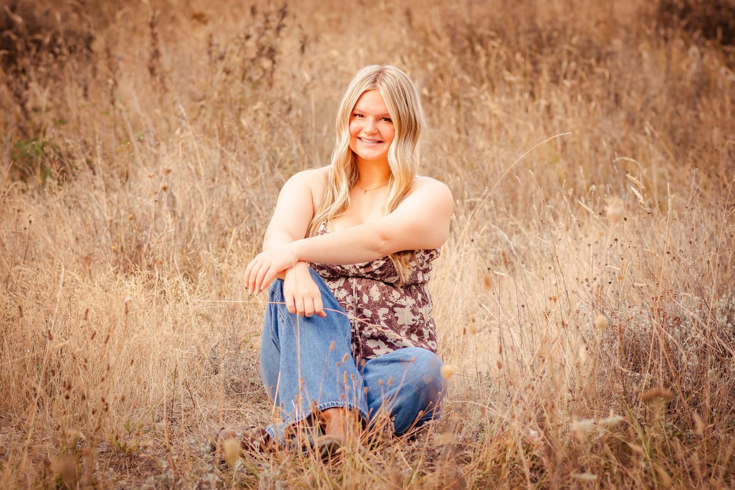 Someone poses in a natural autumn field setting wearing a floral dress and denim during a golden hour photoshoot.