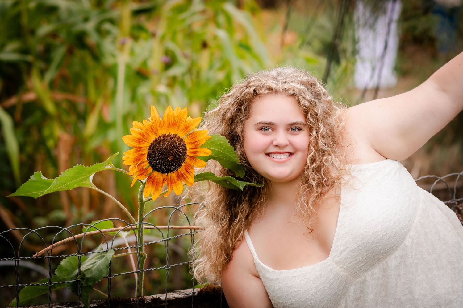 A white strapless wedding dress is photographed in a garden setting with blooming sunflowers.