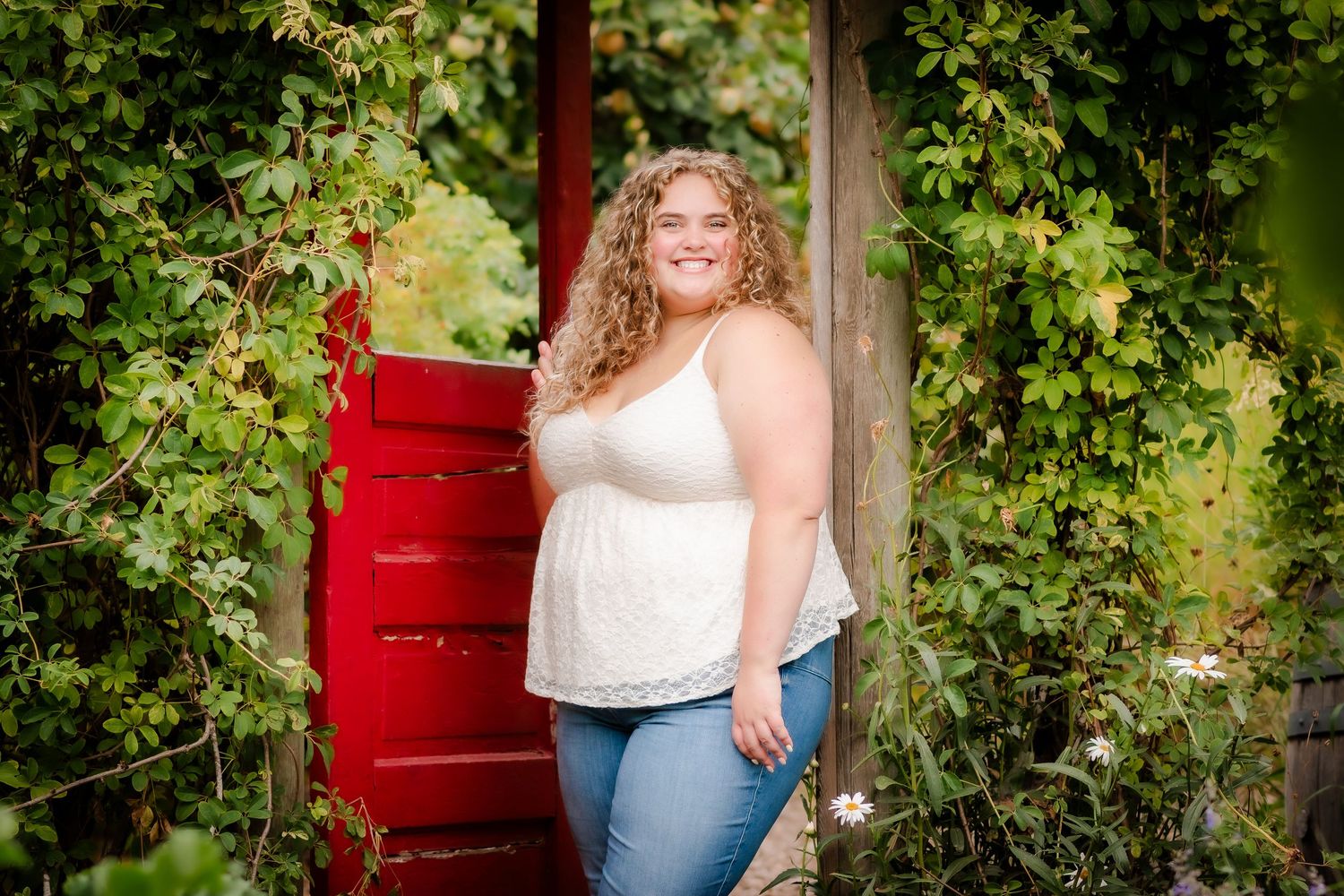 A person poses in casual attire against a backdrop of vibrant green foliage and a red bench in an outdoor setting.