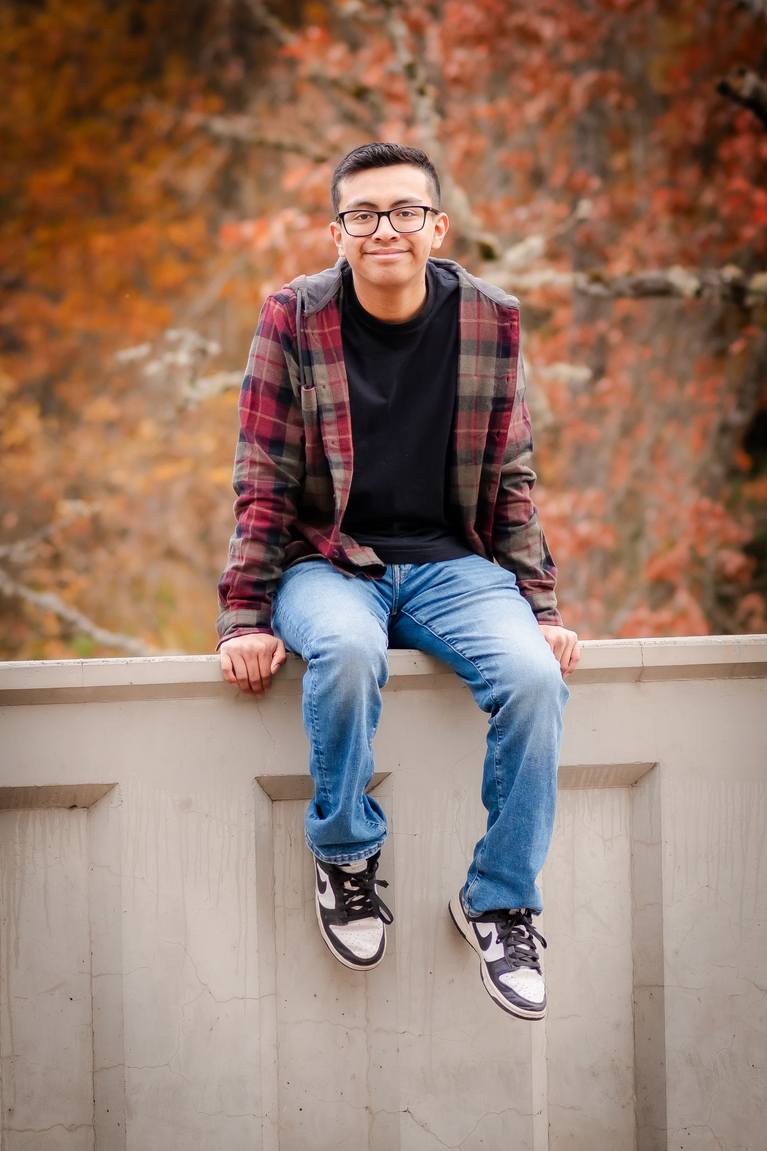 Casual portrait of person in plaid jacket sitting on concrete wall.