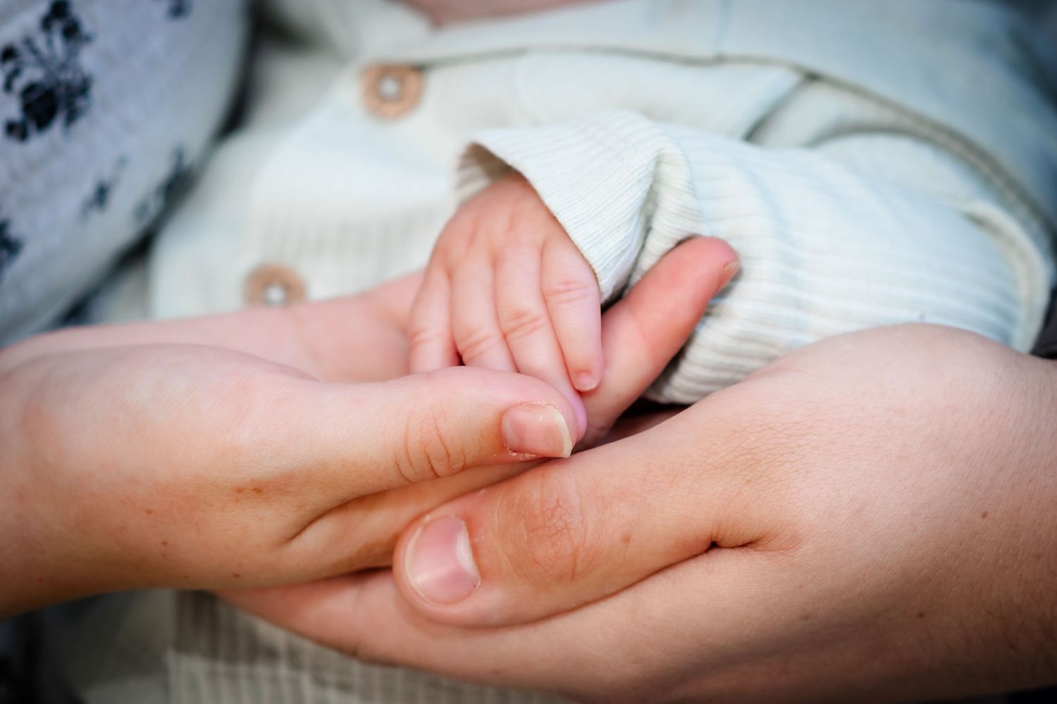 Close-up of a newborn baby's tiny hand gently gripping an adult's finger, symbolizing love and new life.